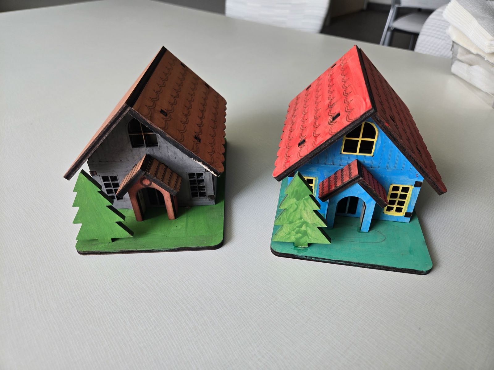 Two hand-painted plywood cottages with red and brown roofs, visible laser-cut edges and trees on green bases
