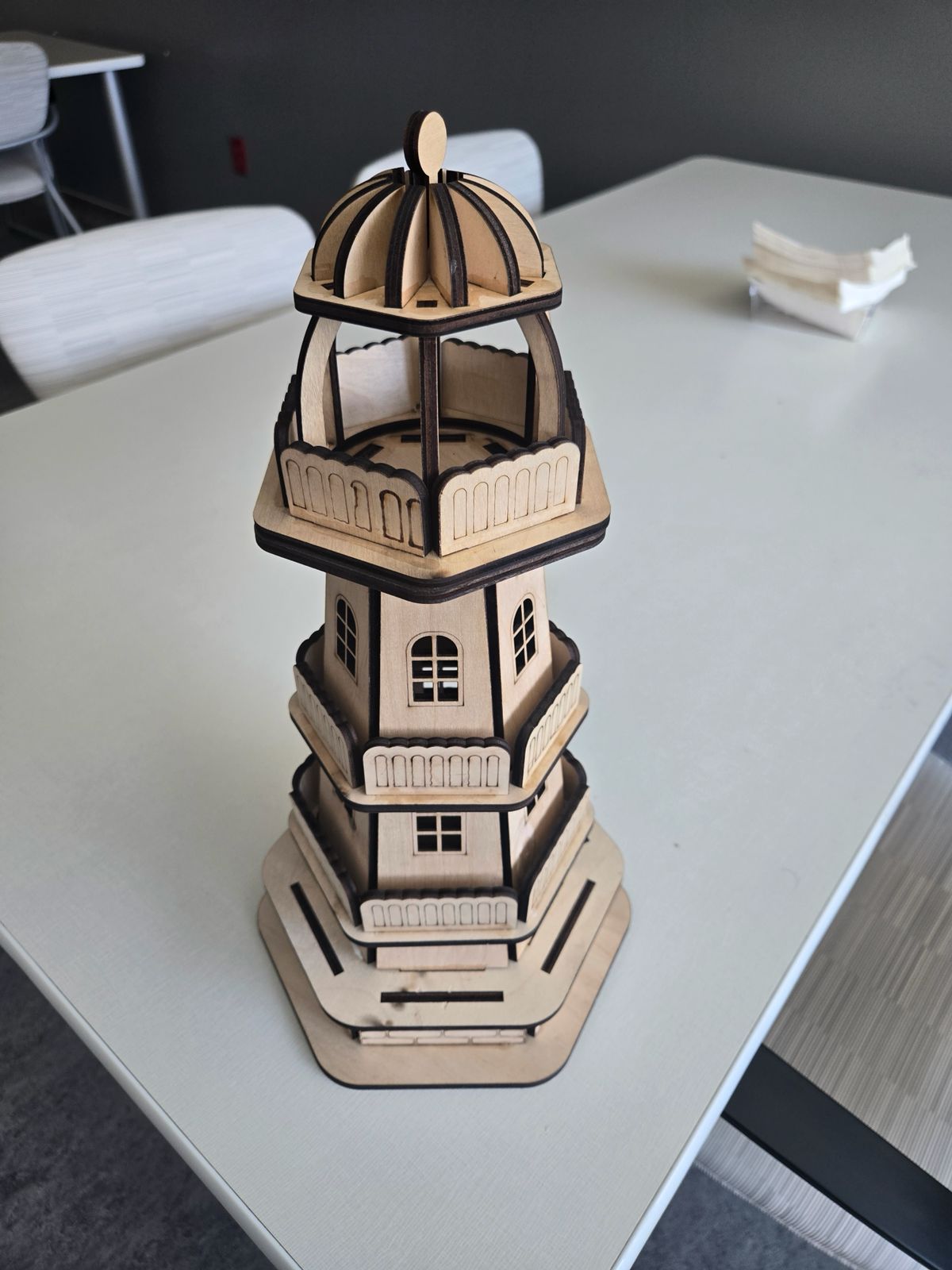 Unpainted plywood tower with balconies, a domed top and dark laser-cut edges